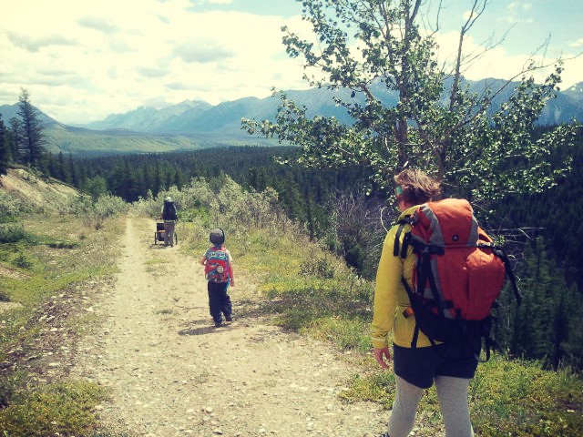 a family bakpacking with kids on a hiking trail carrying large packs and pushing a chariot