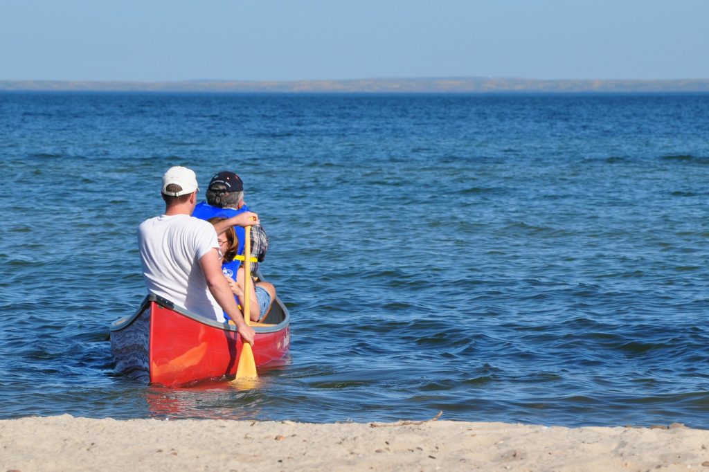 some people in a red canoe paddling away from shore on a deep blue lake