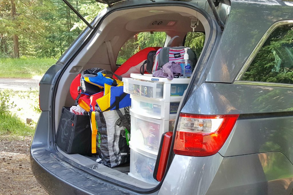 a van trunk open to show family camping gear all packed and organized in bags and tubs