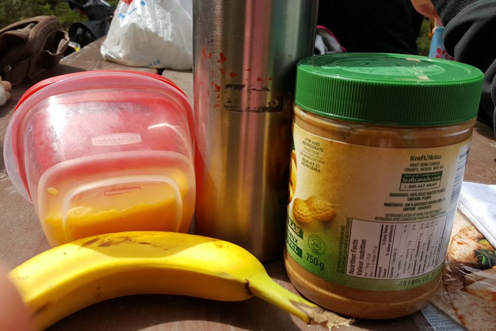 Making easy picnic foods with a banana, peanut butter, wraps on a picnic table