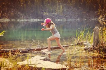a young girl barefooted hoping across rocks in a lake