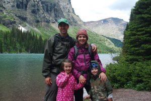 A smiling family out hiking with mountains and a lake in the background