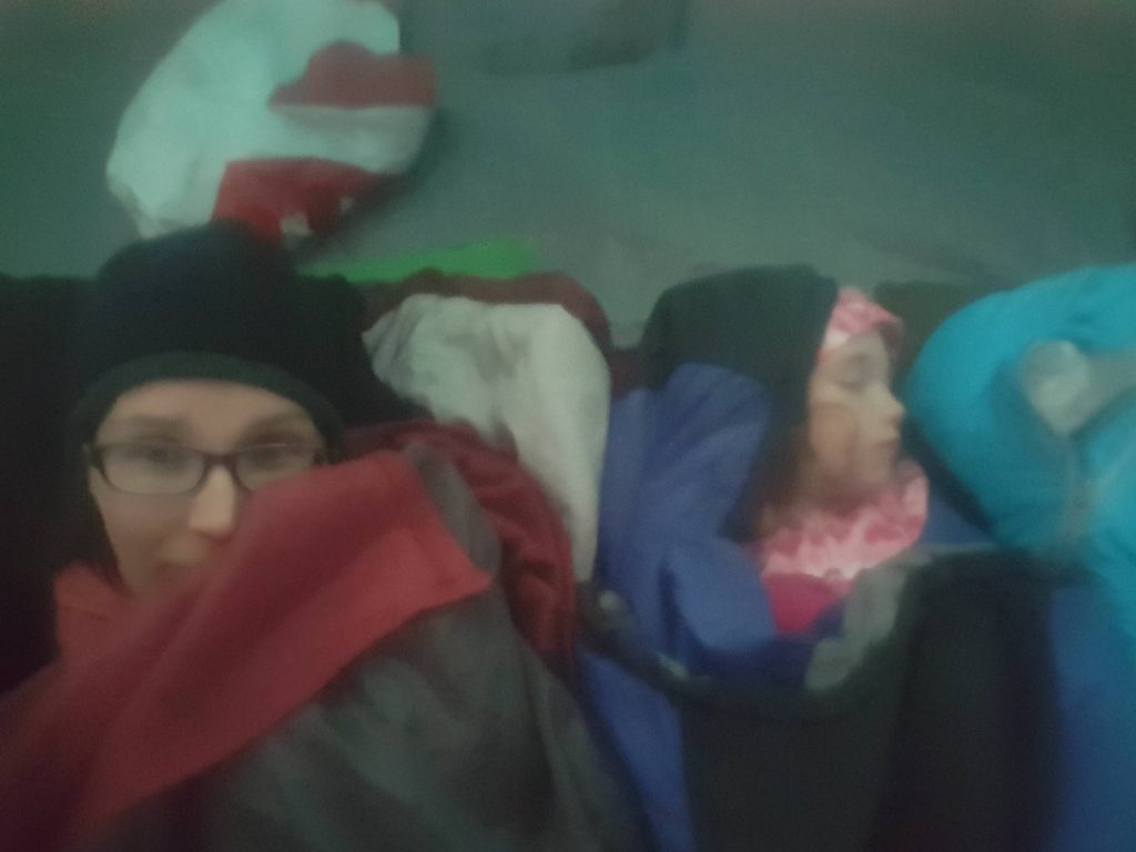 a selfie of a mom and toddler all bundled up in sleeping bags in a tent