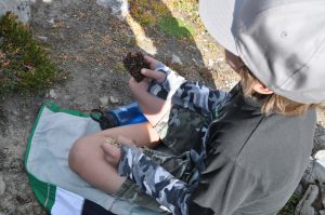 A boy sitting on the rocky ground eating a chocolate snack