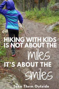Girl with a stick walking on a muddy path, text reads hiking with kids is not about the miles it's about the smiles