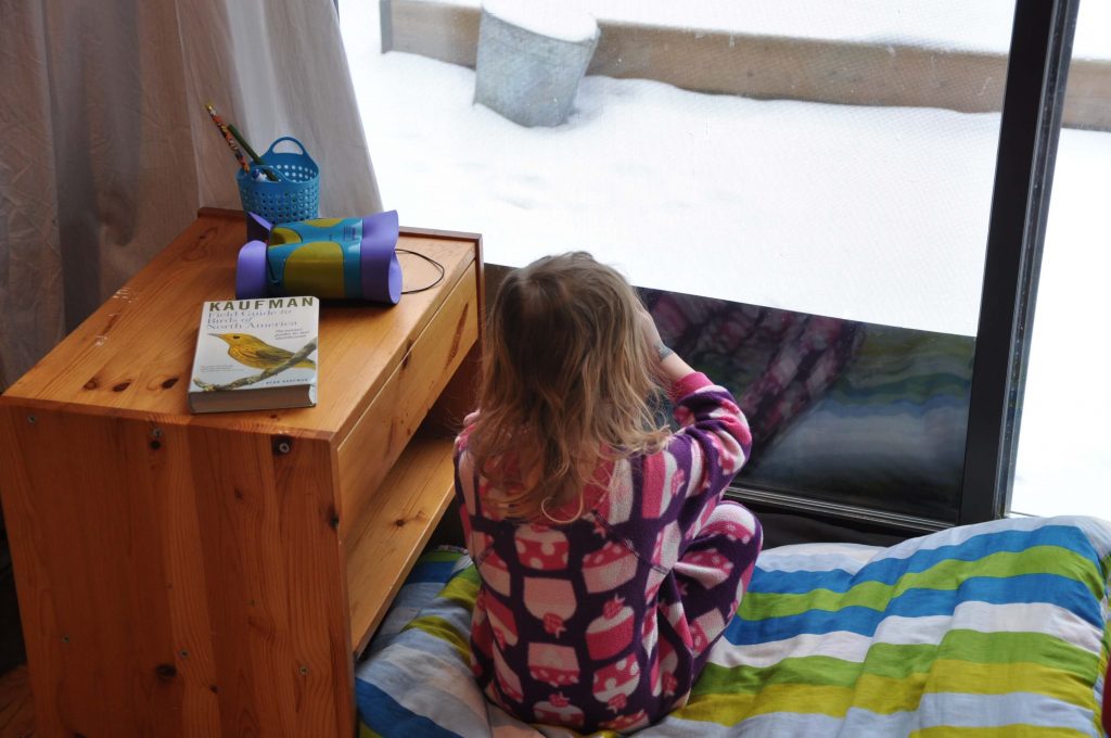 A preschooler sitting on the floor birdwatching out the window