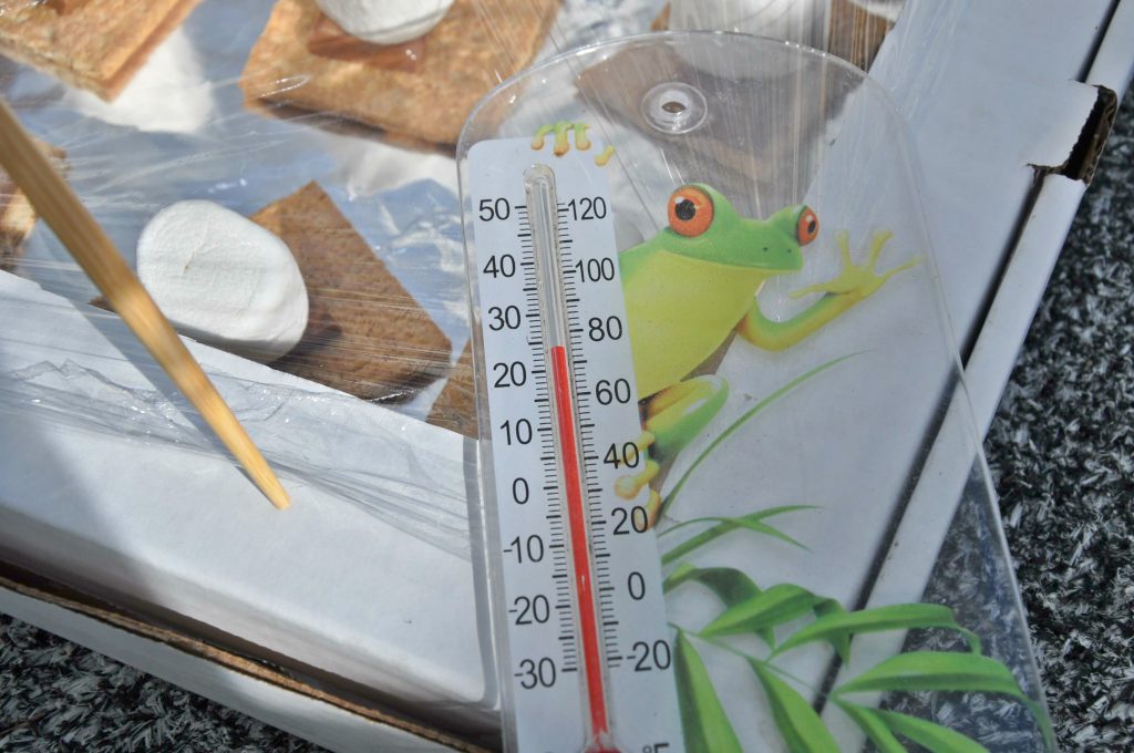 smores cooking in a solar oven with a frog thermometer reading the outdoor temperature