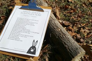 a clipboard holding a nature scavenger hunt sitting on the ground against a log