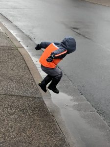 A young child leaping into the air over a puddle