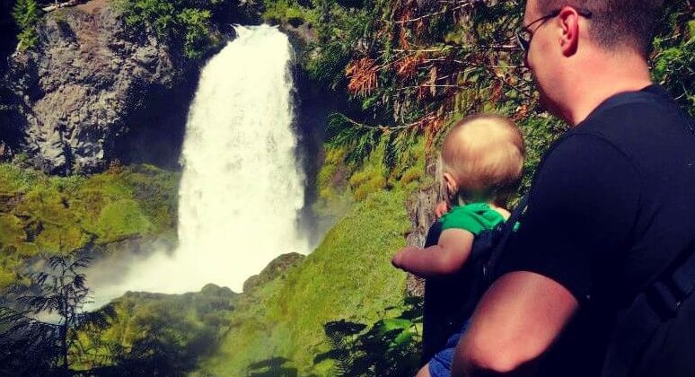 A man holding an infant overlooking a waterfall