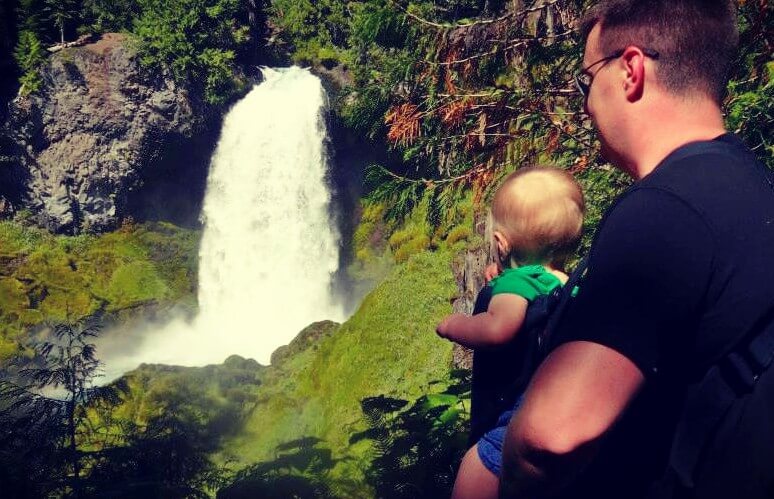 A man holding an infant overlooking a waterfall