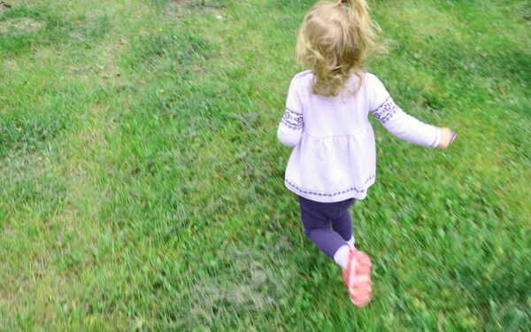 Toddler wearing a white sweater running on the grass