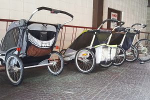 Three all-terrain strollers (Chariots) parked outside a brick building