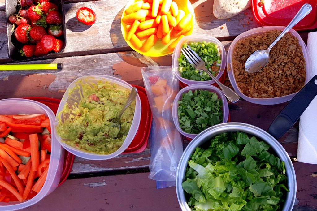 individual containers of taco in a bag toppings: guacamole, lettuce, ground meat, green onions