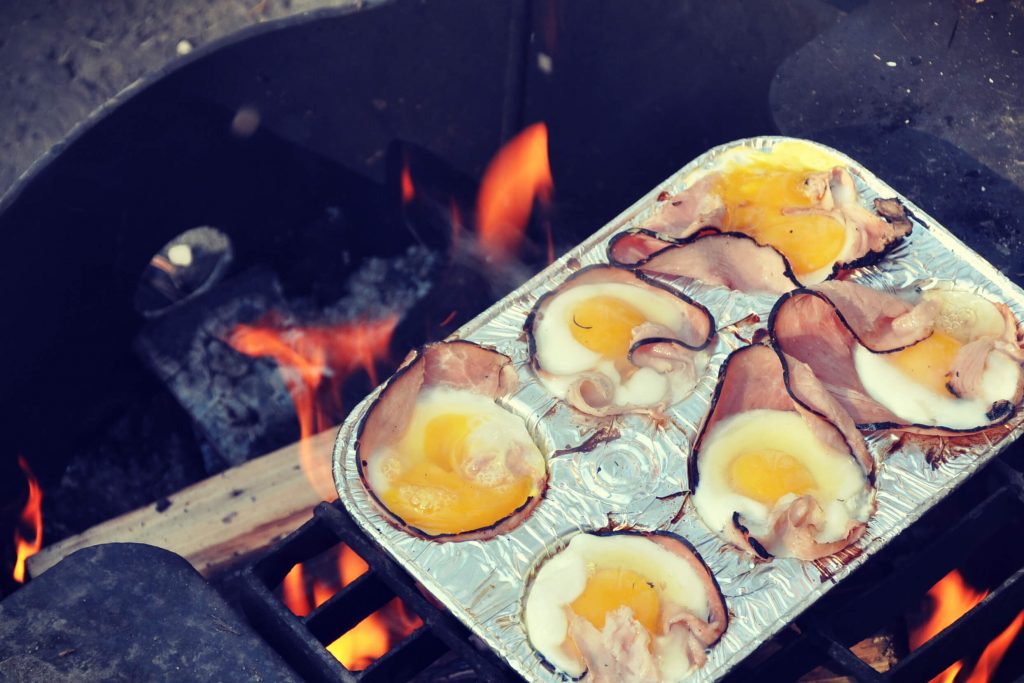 ham and eggs in muffin tins cooking over a campfire