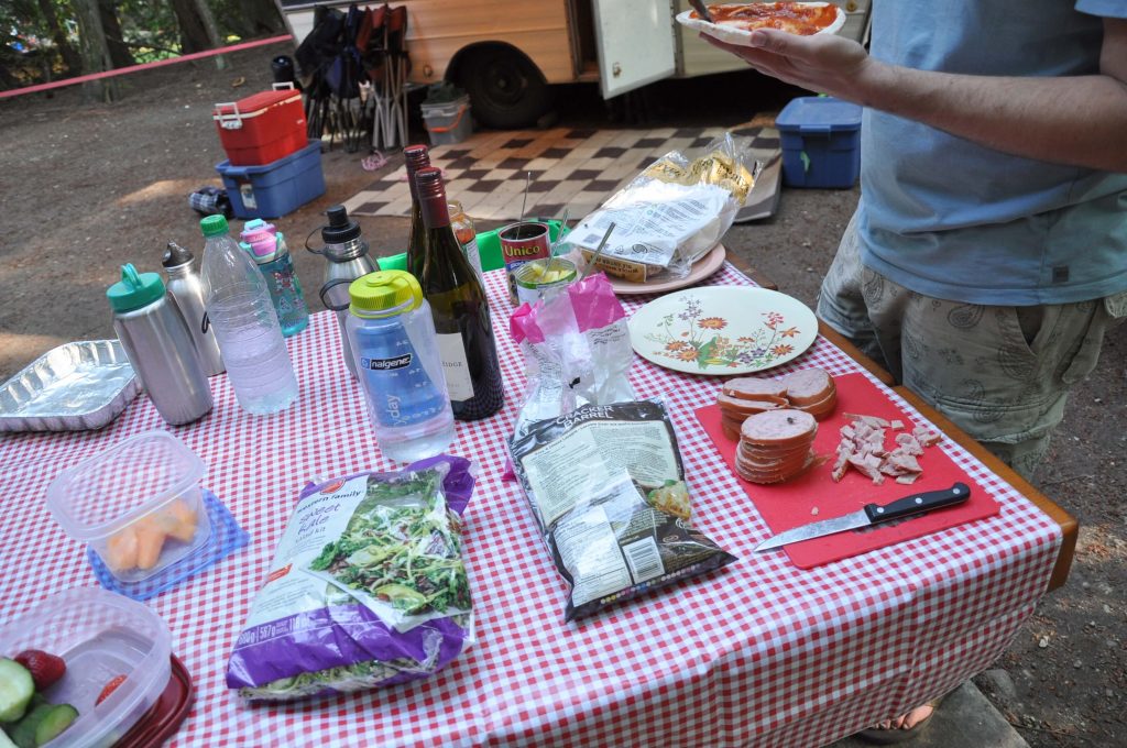 A campground picnic table covered with food supplies to make pita pizzas for dinner