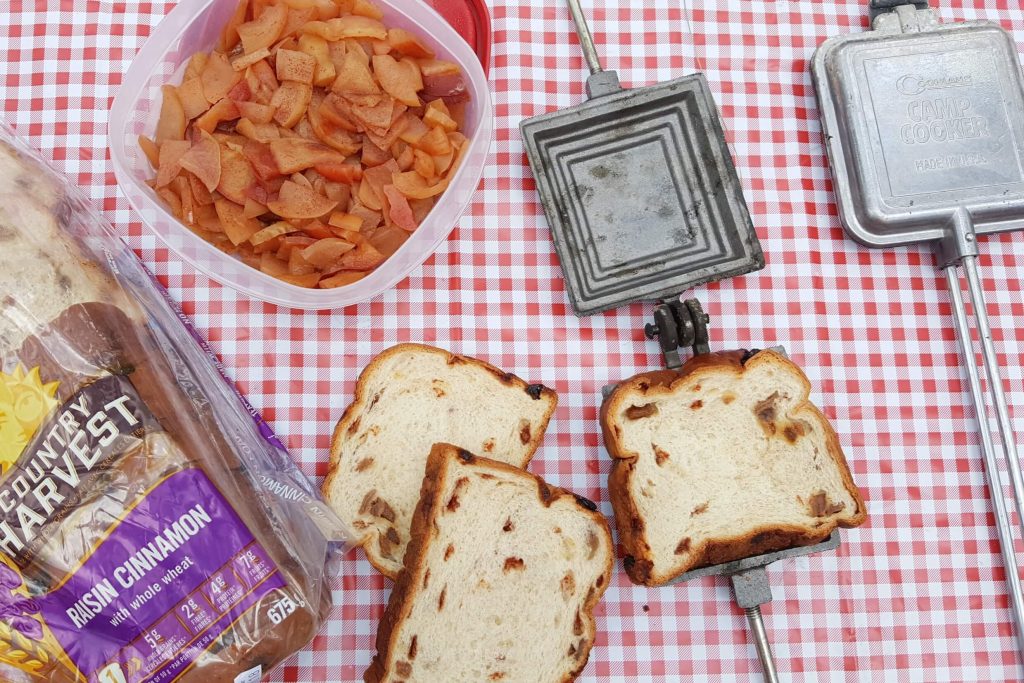 supplies to make campfire apple pies, bread, stewed apples, pie irons all on a red checkered picnic table