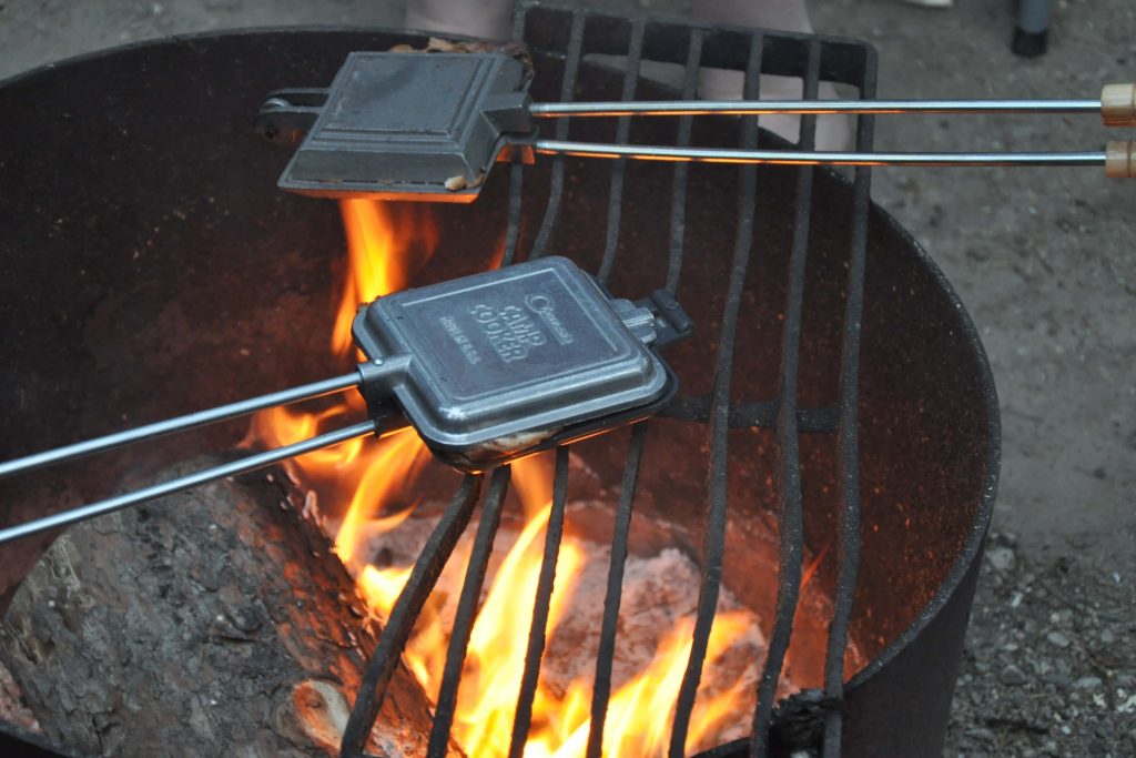 Two pie irons held over a campfire