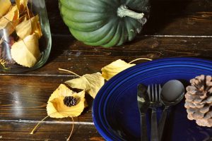 a blue plate, cutlery, some leaves, and a squash all atop a wooden table