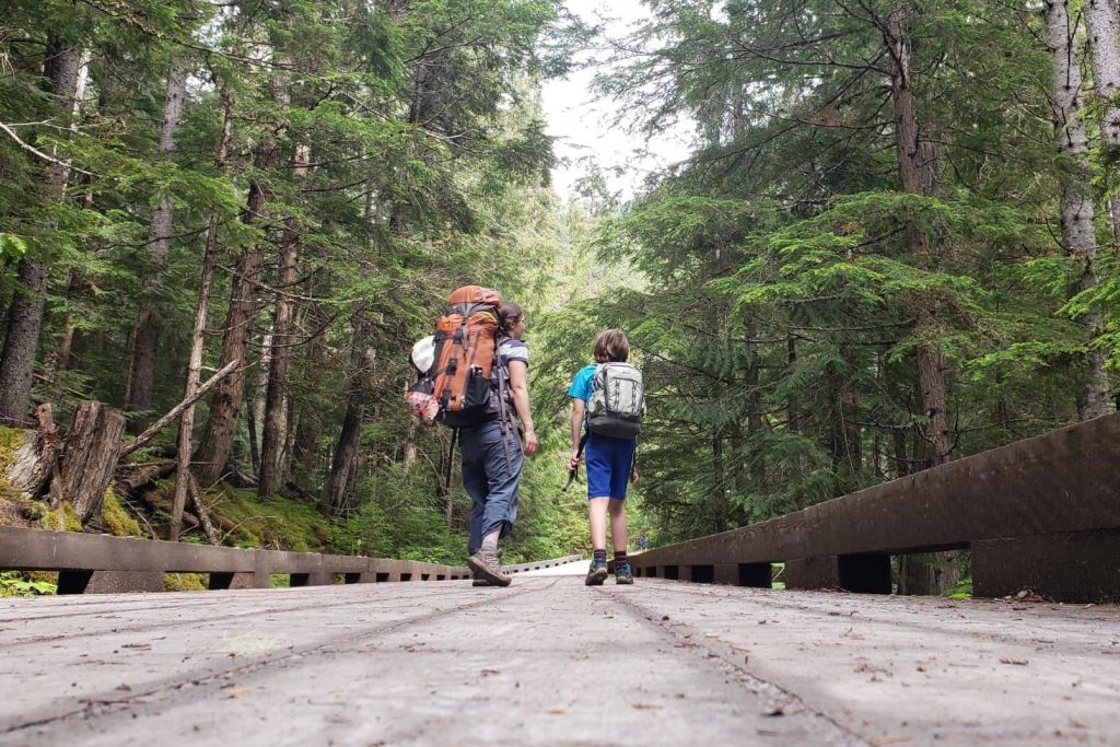 a mom and boy wearing backpacks hiking in the woods