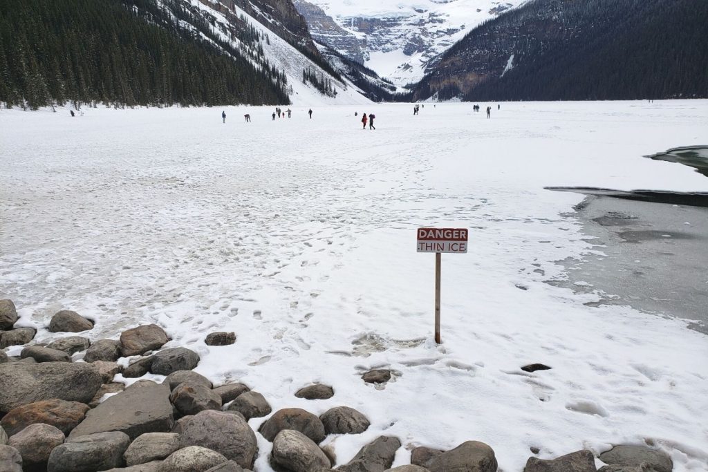 people walking on a frozen lake Lake louise with a danger thin ice sign