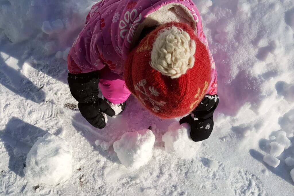 a toddler wearing a pink snowsuit making snowballs in the snow