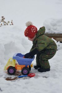 a toddler wearing a green one-piece snow suit playing with toys in the snow