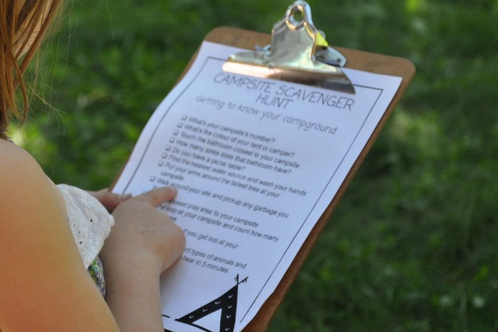 a girl holding a printable camping scavenger hunt on a clipboard