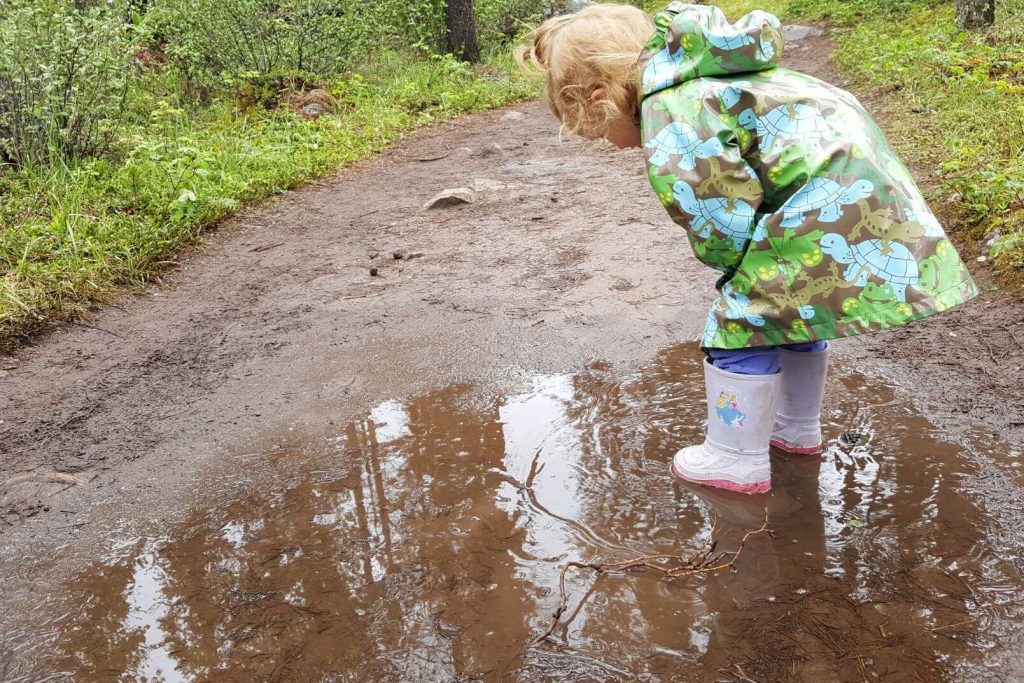 a 2 year old wearing a rain jacket standing in a puddle