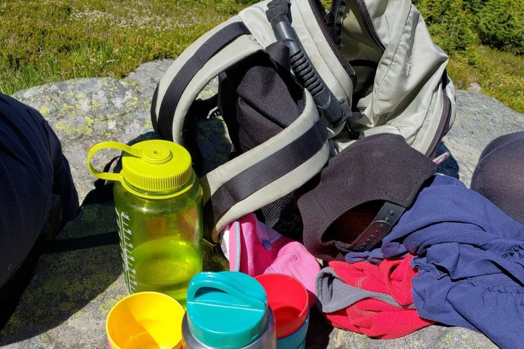 a day pack, water bottles, and jackets sitting on a large rock