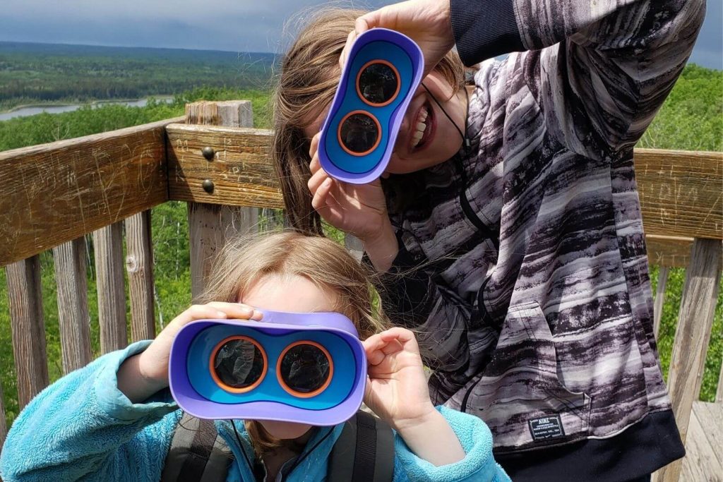 2 kids looking at the camera through kids binoculars