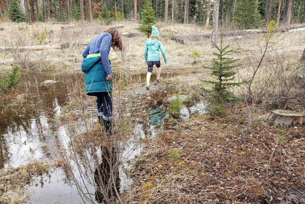 2 kids playing outside in a large puddle in the rain