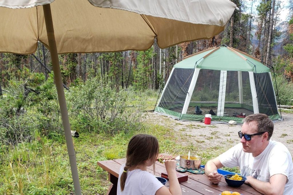 A patio umbrella being used at the campsite to keep rain off the picnic table