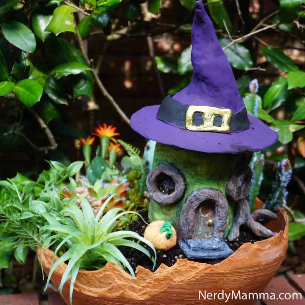 a handmade clay fairy house with a purple witch's hat as the roof