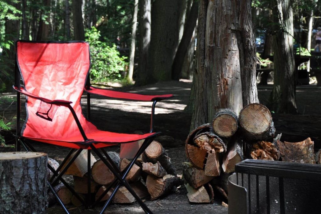 a red camping chair sitting by a pile of logs at a dark, wooded campsite