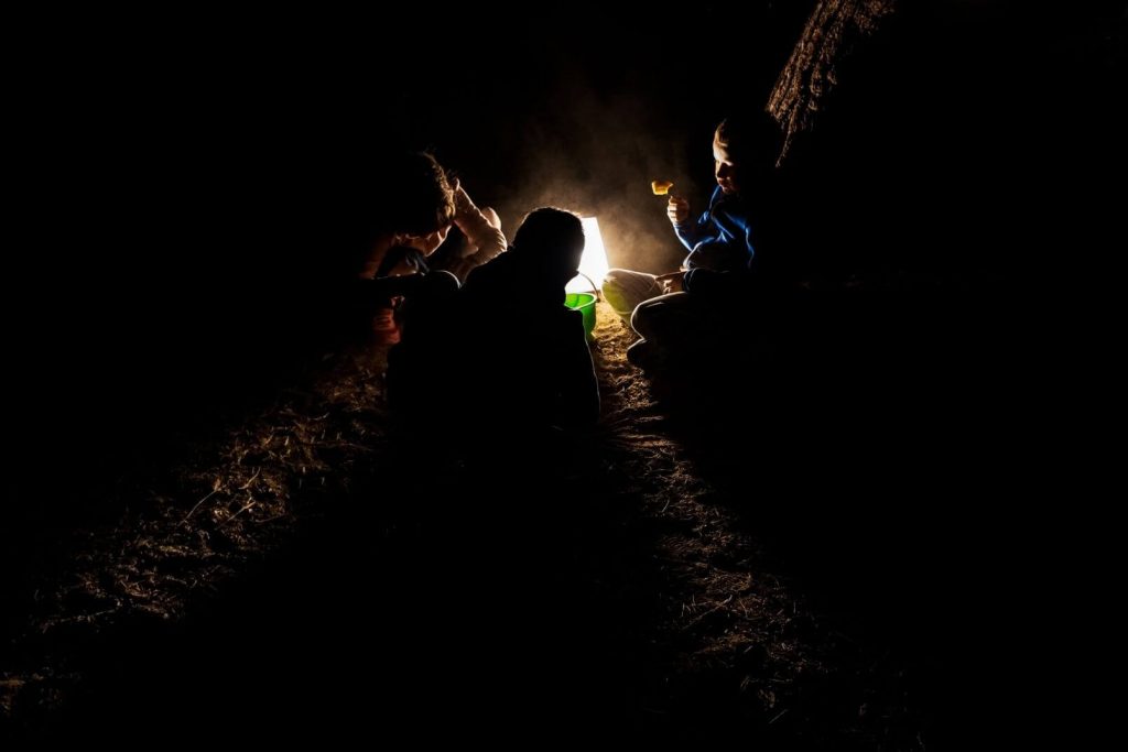 kids playing outside huddled around a lantern in the dark