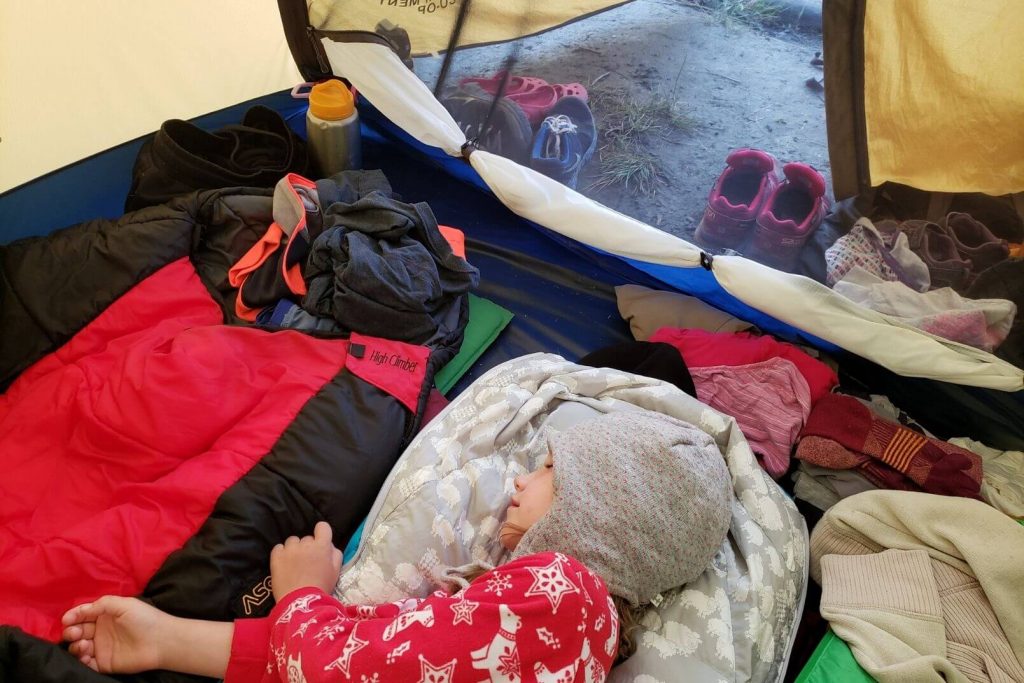 a child wearing a toque sleeping in a tent in a sleeping bag