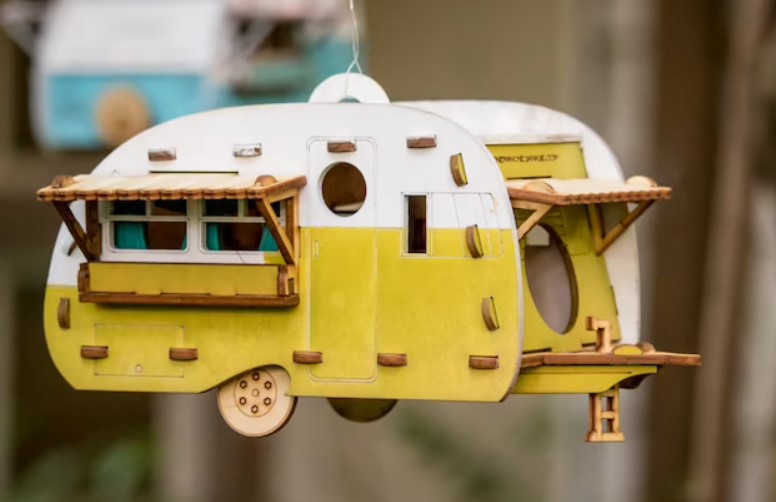 a yellow wooden handmade camper birdhouse hanging in a tree