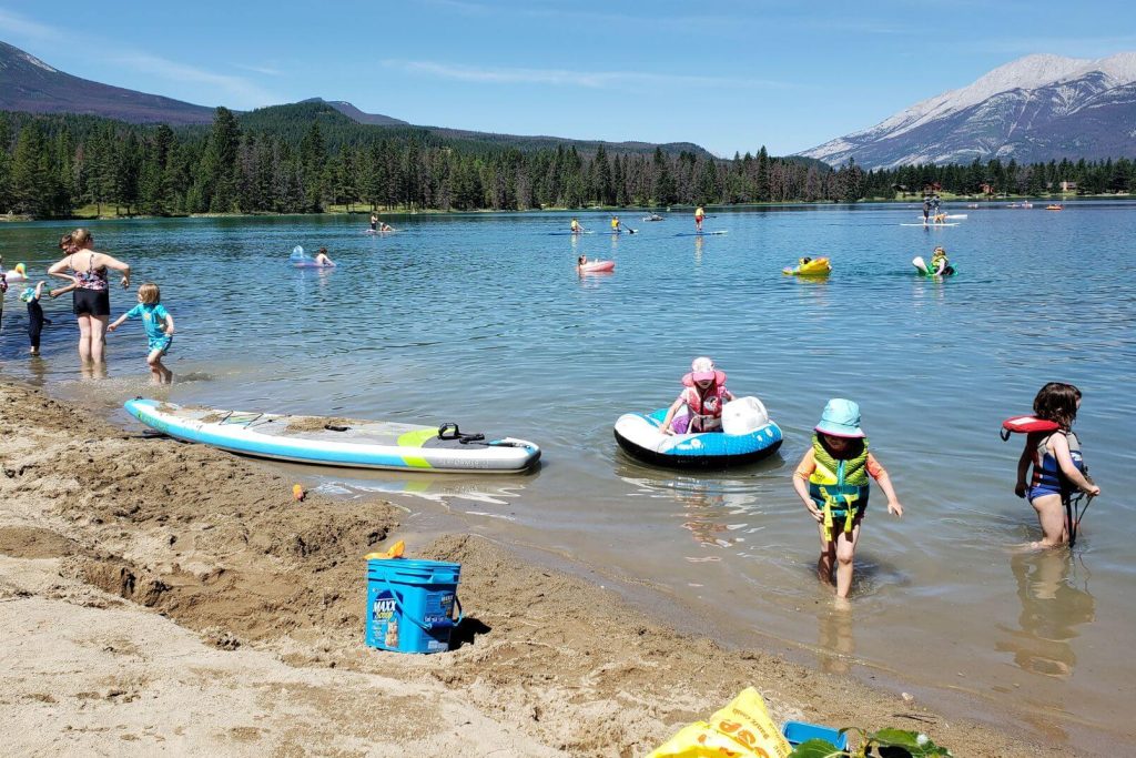 kids and families playing at the beach with kayaks, paddleboards, shovels, and buckets
