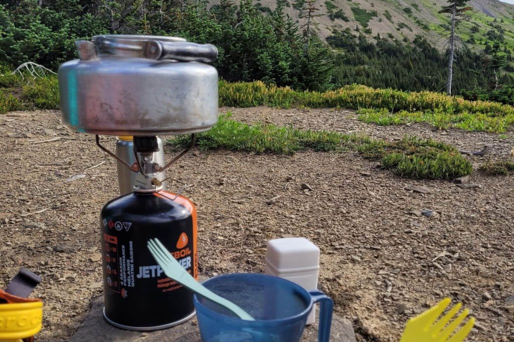 using a camp stove to boil water in a tea kettle when hiking
