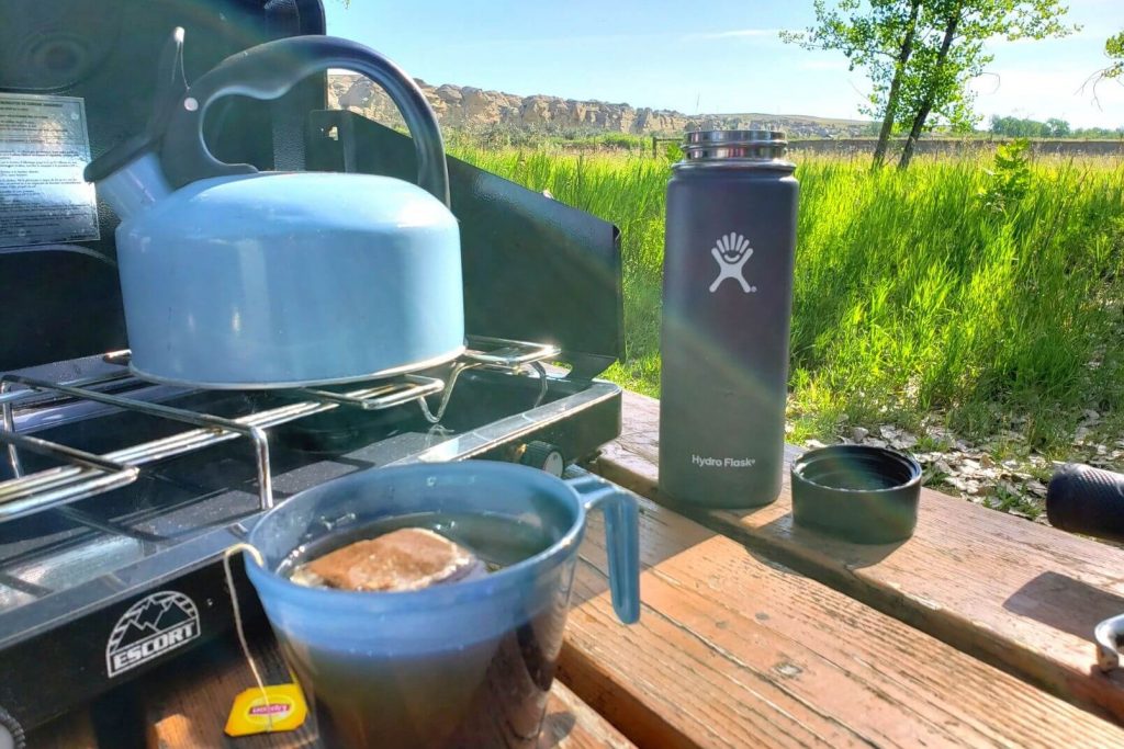 a camping stove with a blue kettle sitting on a picnic table