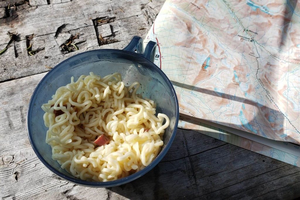 a cup of noodles beside a map on a picnic table
