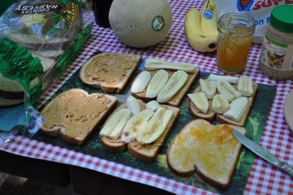 making peanut butter and banana sandwiches on a camping picnic table