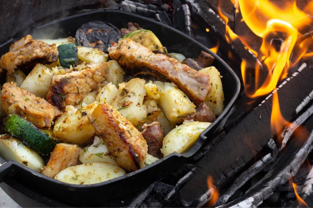 chicken ad vegetables cooking in a cast iron skillet over a campfire