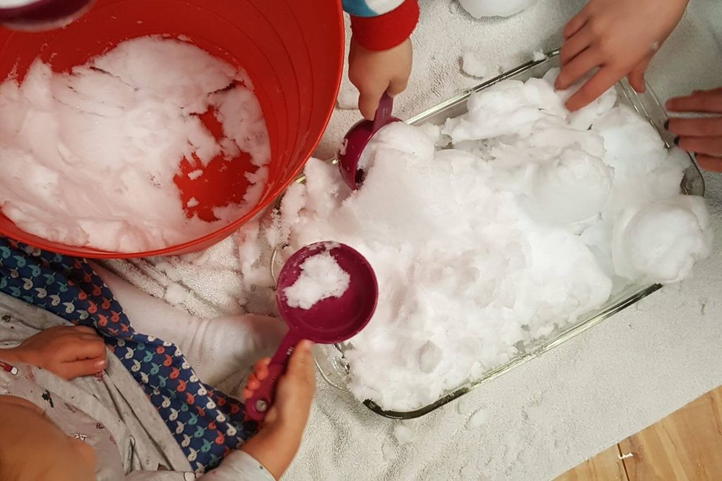 toddlers playing in a bin of snow with measuring spoons