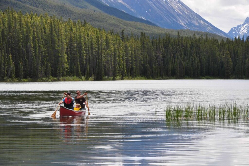 Family canoeing in a red canoe on a lake surrounded by trees and mountains