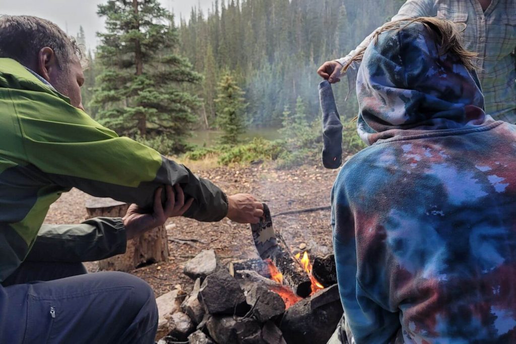 people holding socks over the campfire at the campsite