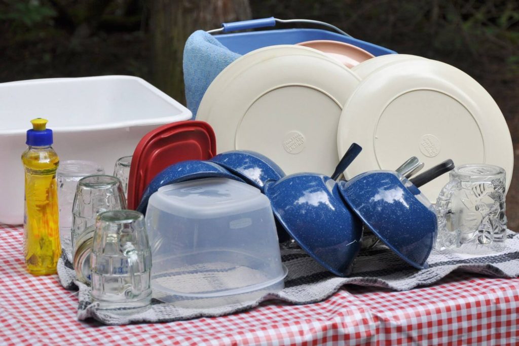 Camping dishes stacked to dry on a red checkered picnic table cloth