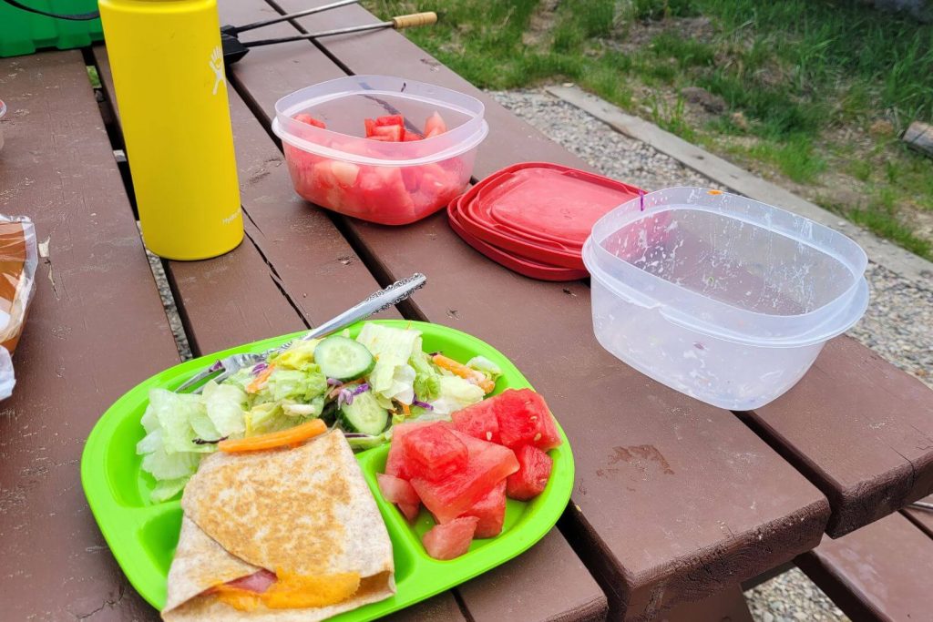 A Simple Camping lunch sitting on a picnic table: grilled cheese, fruit, and salad