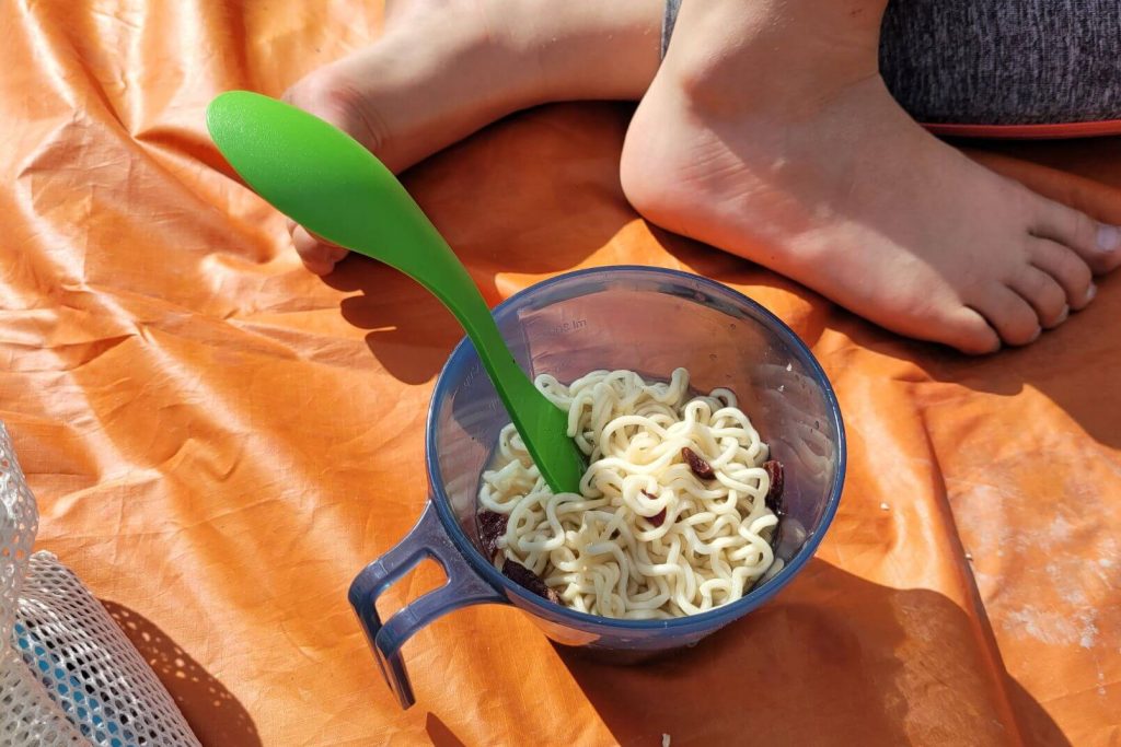 instant noodles in a camping cup on an orange ground tarp